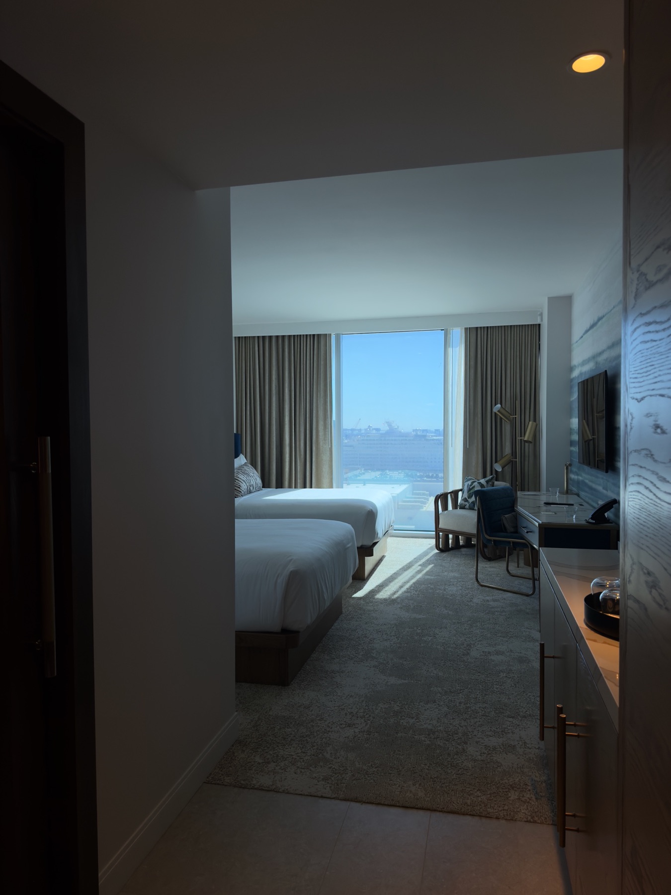 Sunlit hotel room viewed from the entry with a city view beyond